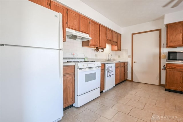 kitchen with backsplash, under cabinet range hood, light countertops, white appliances, and a sink