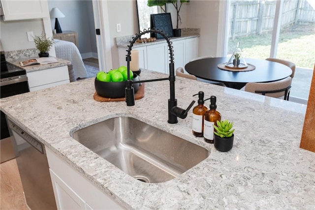 kitchen with white cabinetry, light stone counters, dishwasher, and a sink