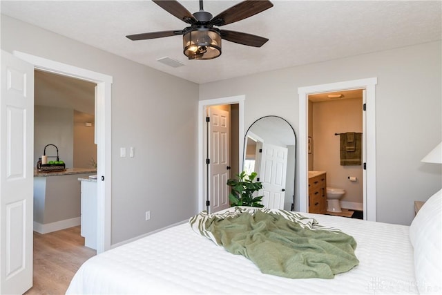 bedroom with light wood-type flooring, visible vents, a ceiling fan, ensuite bathroom, and baseboards