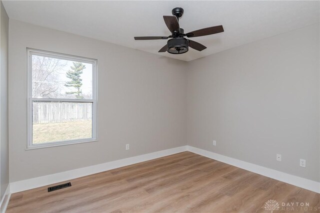 empty room with ceiling fan, visible vents, baseboards, and wood finished floors