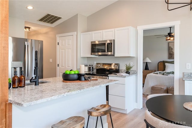 kitchen featuring light stone countertops, visible vents, a peninsula, stainless steel appliances, and white cabinetry