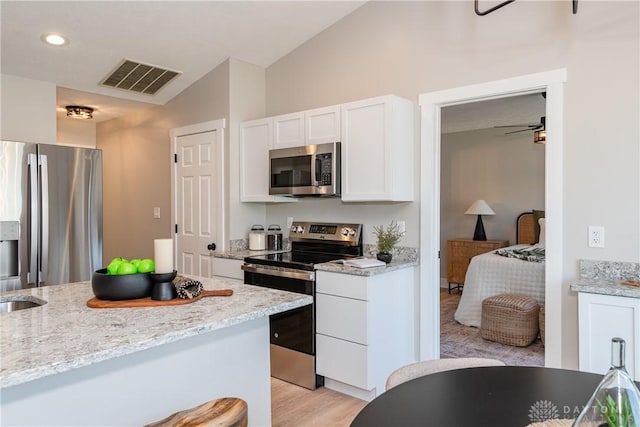 kitchen featuring light stone counters, visible vents, lofted ceiling, stainless steel appliances, and white cabinets