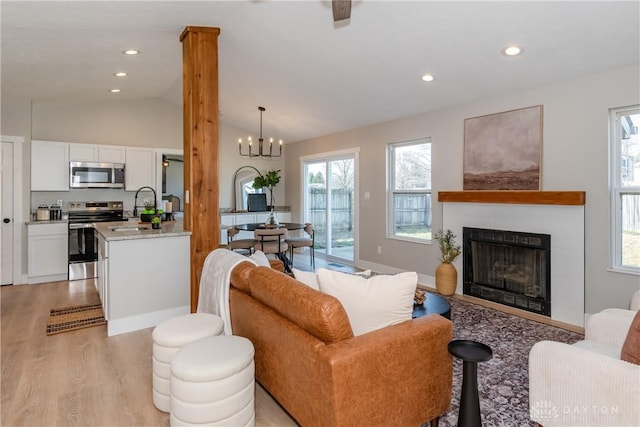 living room featuring recessed lighting, a fireplace, vaulted ceiling, a notable chandelier, and light wood-type flooring