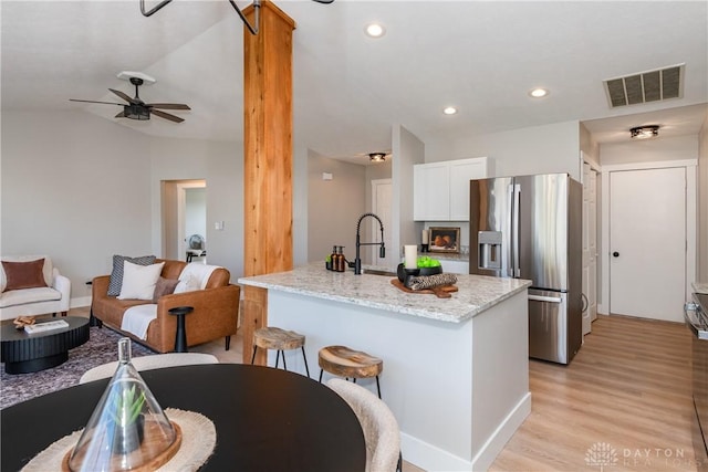 kitchen with light stone countertops, visible vents, white cabinets, stainless steel refrigerator with ice dispenser, and light wood-type flooring