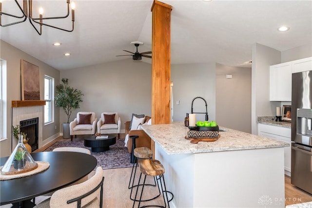 kitchen featuring light wood-style flooring, a kitchen island, white cabinetry, stainless steel fridge, and a fireplace