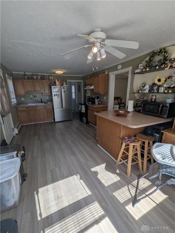 kitchen with brown cabinetry, stove, black microwave, and freestanding refrigerator