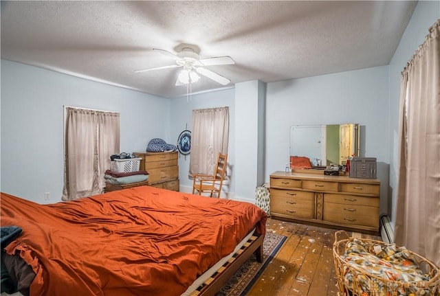 bedroom with a baseboard heating unit, wood-type flooring, a textured ceiling, and ceiling fan