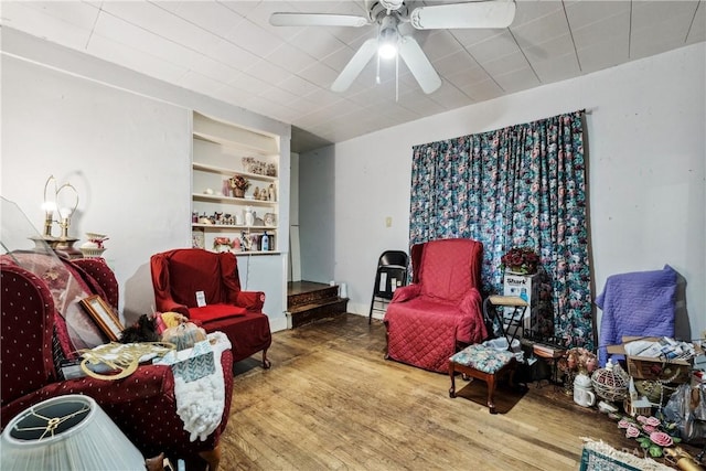 sitting room with built in shelves, wood finished floors, and a ceiling fan