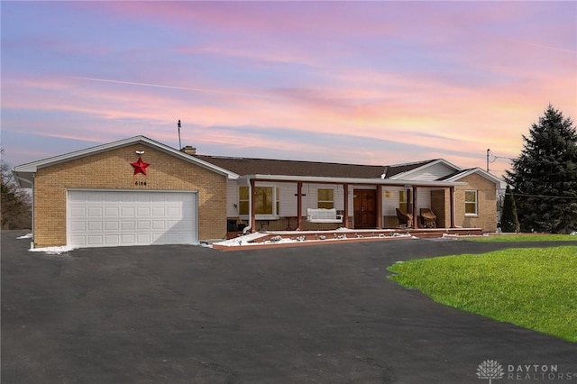 ranch-style house with driveway, brick siding, a garage, a porch, and a front lawn