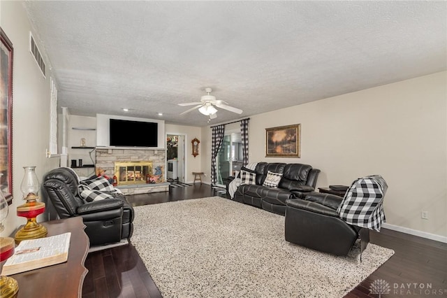 living area with a textured ceiling, ceiling fan, a stone fireplace, wood finished floors, and baseboards