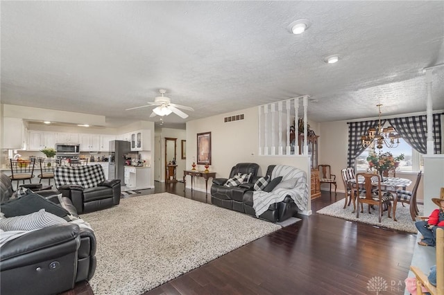 living room with visible vents, a textured ceiling, dark wood-style flooring, and ceiling fan with notable chandelier