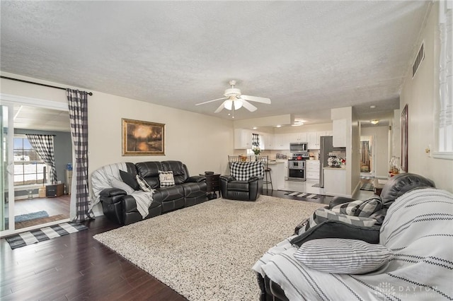 living area featuring visible vents, a textured ceiling, dark wood-style flooring, and a ceiling fan