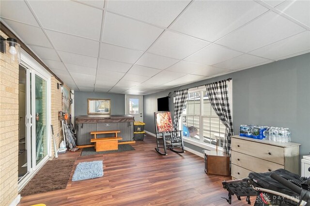 living area featuring baseboards, a paneled ceiling, dark wood-type flooring, and brick wall