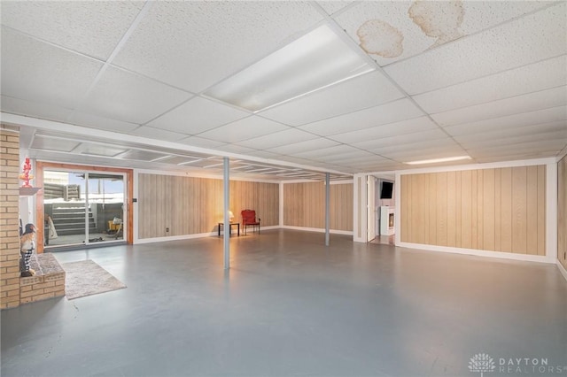 basement featuring a drop ceiling, wood walls, and baseboards