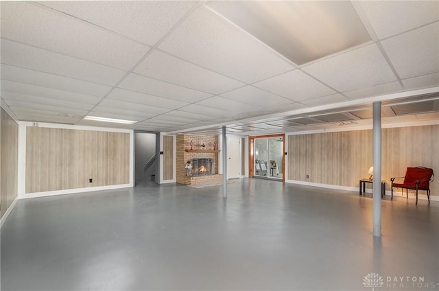 finished basement with baseboards, a paneled ceiling, a brick fireplace, and wood walls