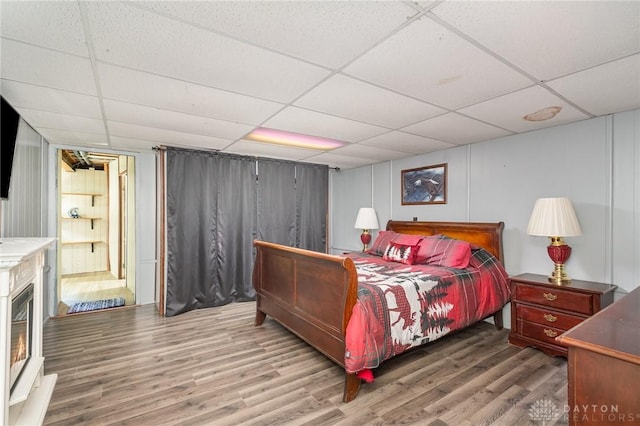 bedroom with a warm lit fireplace, wood finished floors, and a drop ceiling