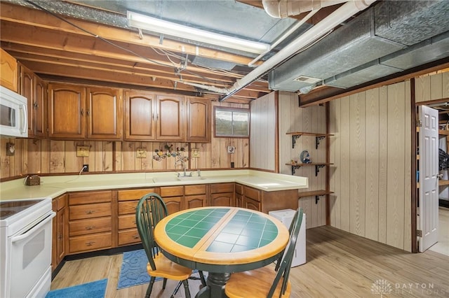 kitchen with wood walls, light wood-style flooring, brown cabinetry, white appliances, and a sink