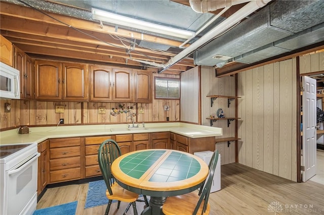 kitchen featuring white appliances, a sink, light wood-style floors, brown cabinetry, and wood walls
