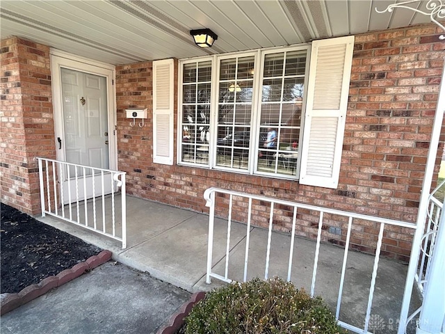 view of exterior entry featuring brick siding and covered porch