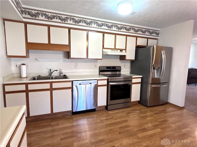 kitchen featuring a sink, under cabinet range hood, wood finished floors, stainless steel appliances, and light countertops