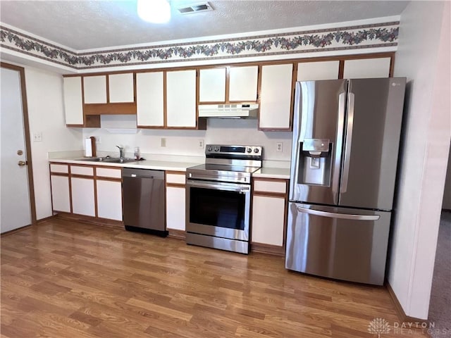 kitchen featuring visible vents, under cabinet range hood, light countertops, stainless steel appliances, and a sink