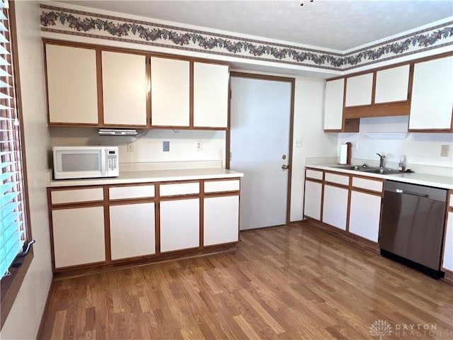 kitchen with light wood finished floors, a sink, stainless steel dishwasher, light countertops, and white microwave