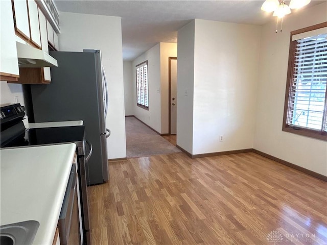 kitchen with light wood-style flooring, baseboards, under cabinet range hood, and stainless steel range with electric cooktop