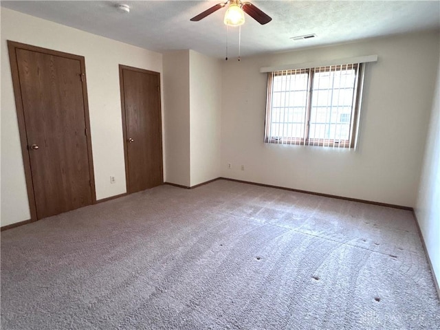 unfurnished bedroom featuring carpet, baseboards, visible vents, a textured ceiling, and two closets