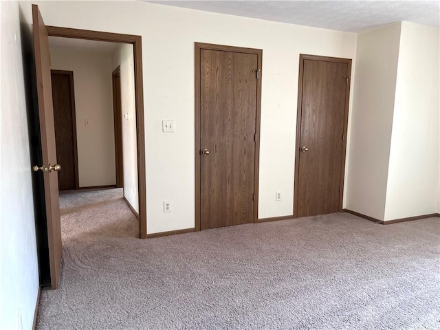 unfurnished bedroom with carpet, baseboards, and two closets