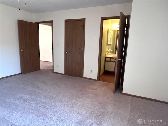 unfurnished bedroom with ensuite bath, baseboards, and carpet floors