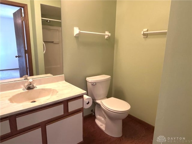 bathroom with baseboards, walk in shower, toilet, wood finished floors, and vanity