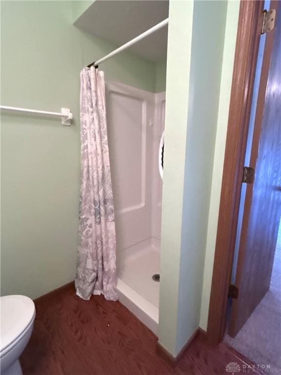 bathroom with wood finished floors, toilet, and a stall shower