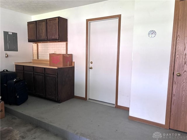 interior space with electric panel, tasteful backsplash, dark brown cabinets, baseboards, and concrete flooring