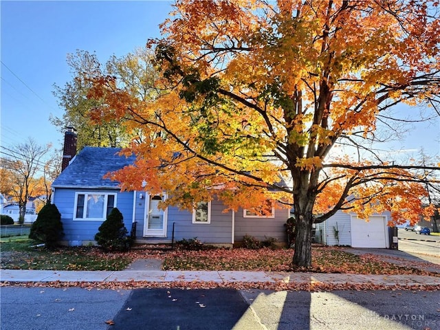 obstructed view of property with an outbuilding, an attached garage, concrete driveway, and a chimney