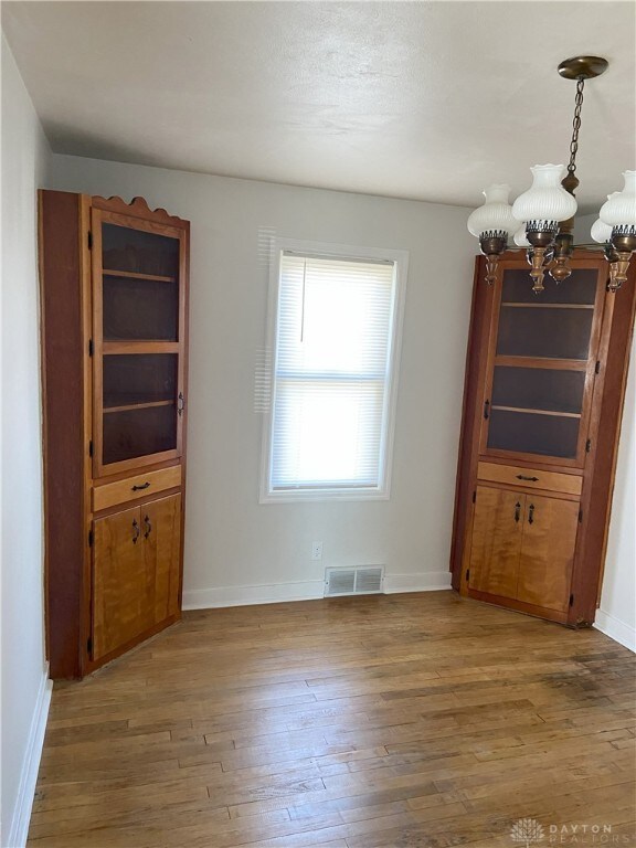 unfurnished dining area featuring an inviting chandelier, wood finished floors, visible vents, and baseboards