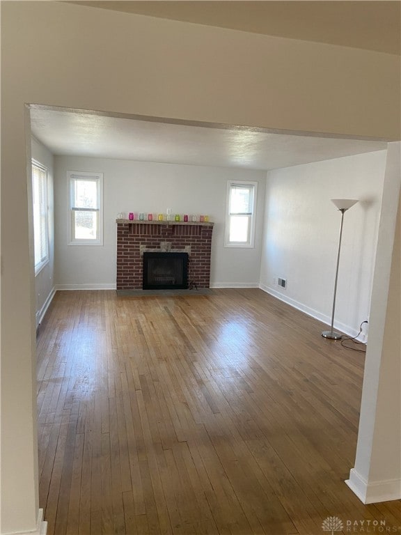 unfurnished living room featuring a wealth of natural light, baseboards, a fireplace, and hardwood / wood-style flooring