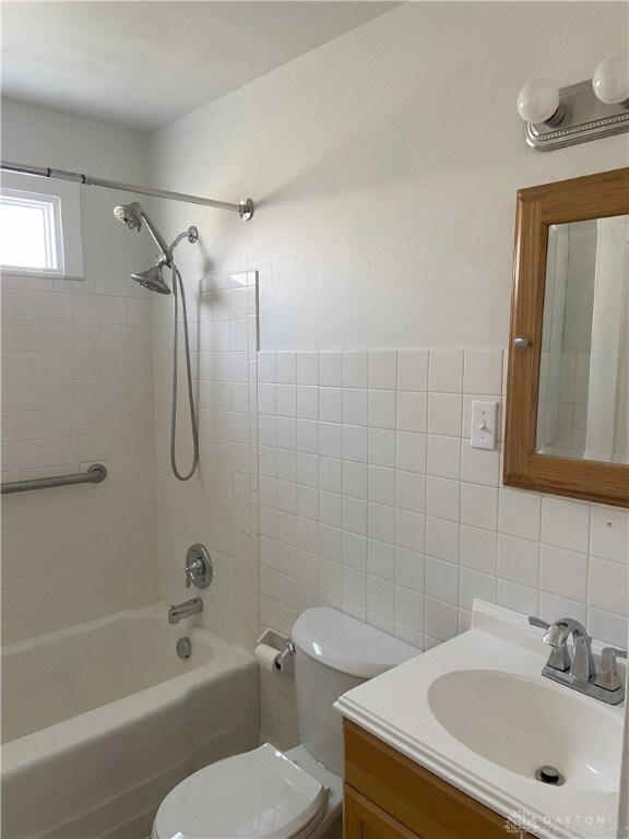 full bath with shower / tub combination, vanity, toilet, and tile walls