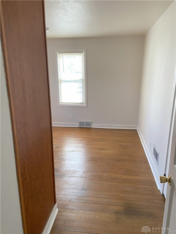 empty room with baseboards, visible vents, and wood-type flooring