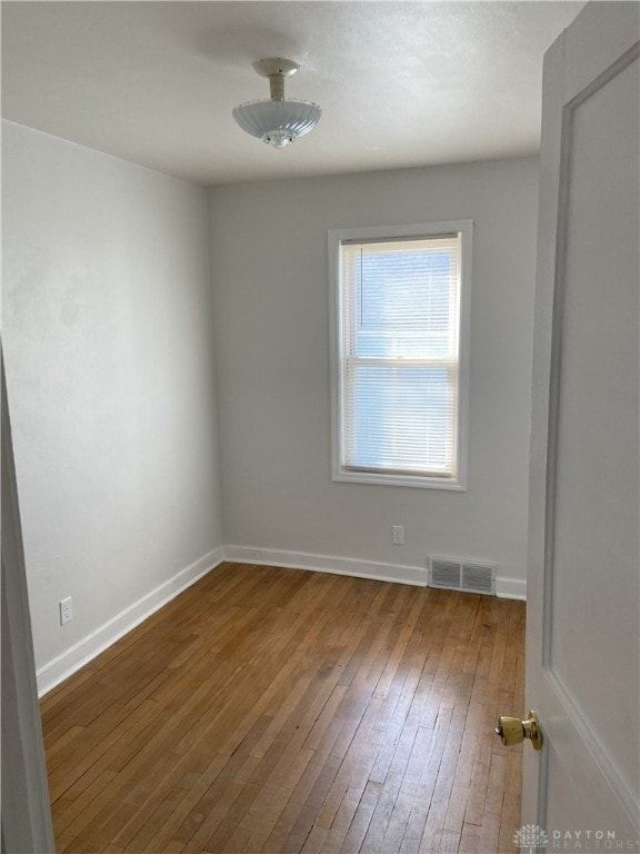 empty room with hardwood / wood-style flooring, baseboards, and visible vents