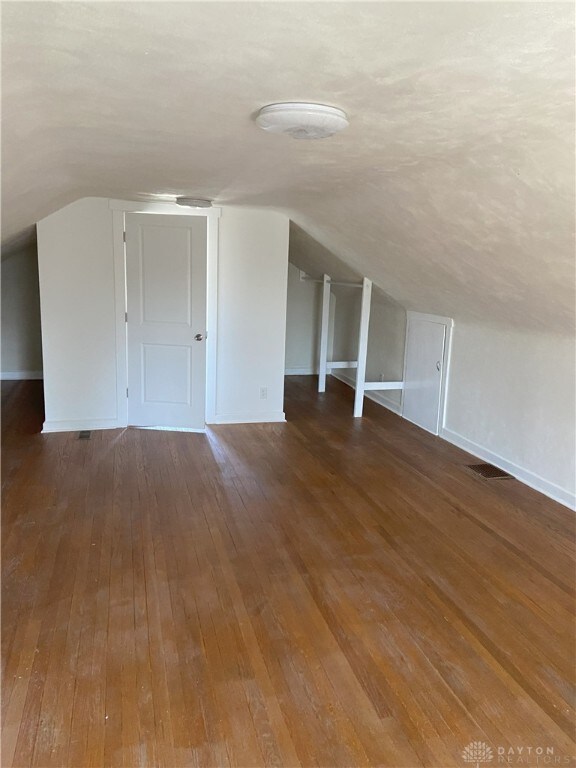 additional living space with baseboards, lofted ceiling, visible vents, and hardwood / wood-style flooring