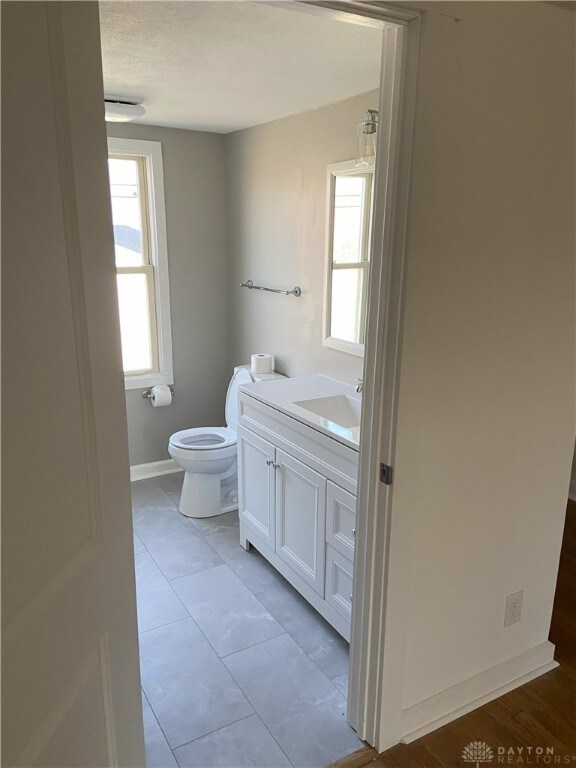 half bath with tile patterned floors, toilet, vanity, and baseboards