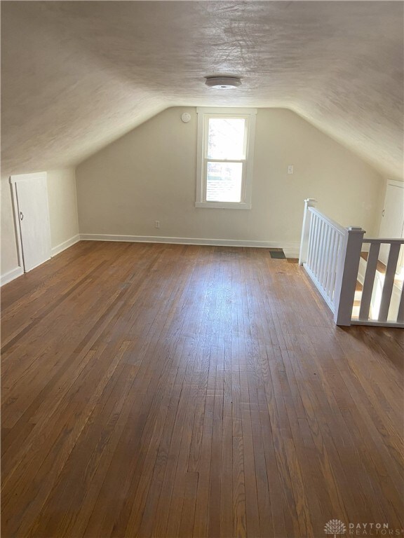 additional living space featuring visible vents, dark wood-type flooring, lofted ceiling, a textured ceiling, and baseboards