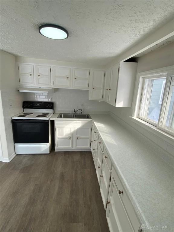 kitchen with white range with electric cooktop, a sink, dark wood-type flooring, white cabinets, and under cabinet range hood