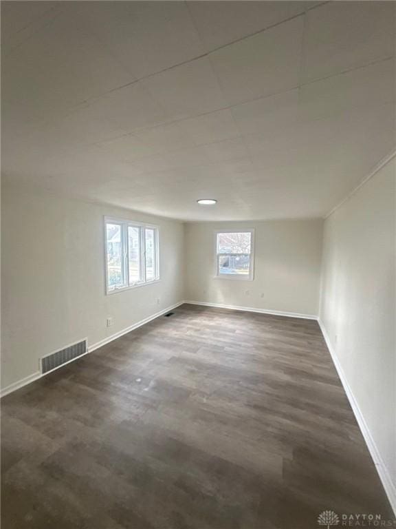 unfurnished room featuring visible vents, baseboards, and dark wood-style floors