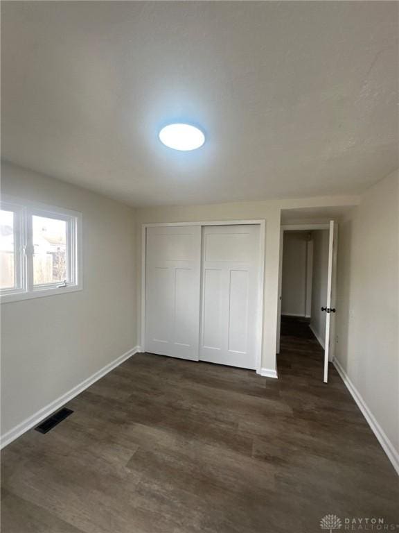 unfurnished bedroom featuring visible vents, baseboards, a closet, and dark wood finished floors