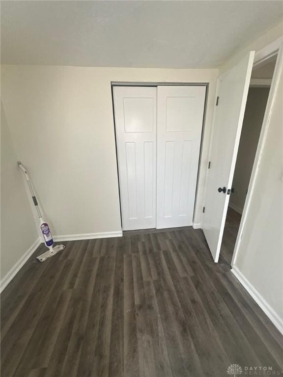 unfurnished bedroom featuring dark wood-style floors, a closet, and baseboards