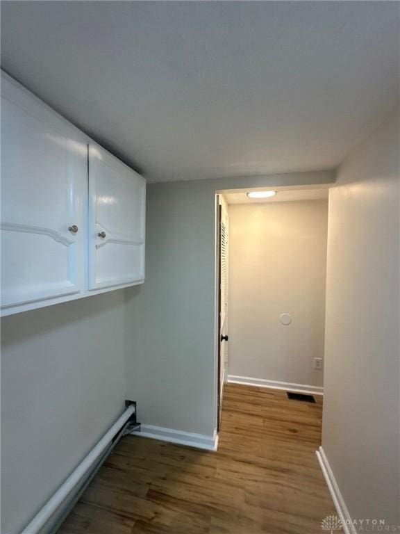 clothes washing area with visible vents, baseboards, and wood finished floors