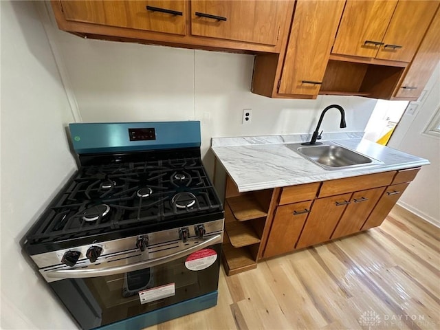 kitchen featuring a sink, stainless steel range with gas cooktop, brown cabinetry, and light countertops