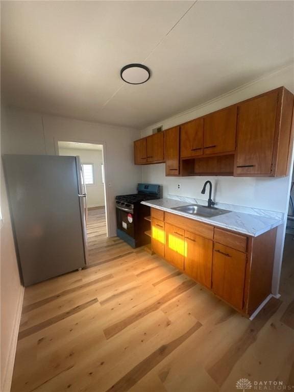 kitchen with brown cabinetry, a sink, stainless steel appliances, light countertops, and light wood-style floors