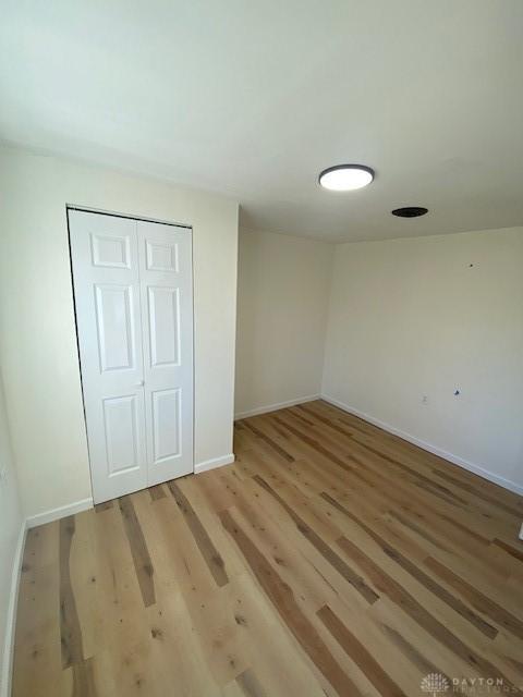 unfurnished bedroom featuring light wood-style floors, a closet, and baseboards